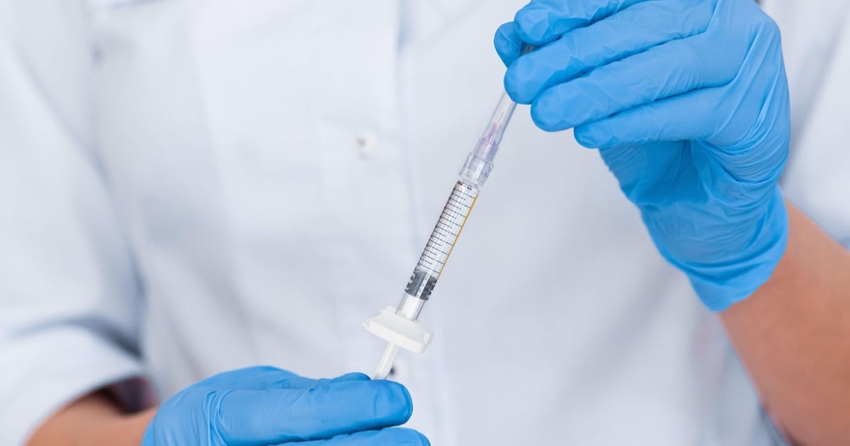 O femeie cu mănuși albastre care ține o injecție în mâini