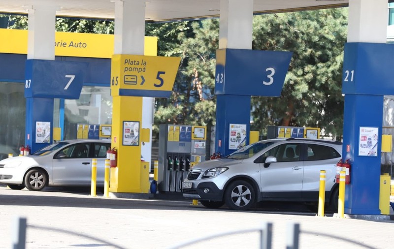 Imaginea prezintă o stație de carburanți cu mai multe pompe numerotate, unde sunt parcate două autoturisme pentru alimentat.