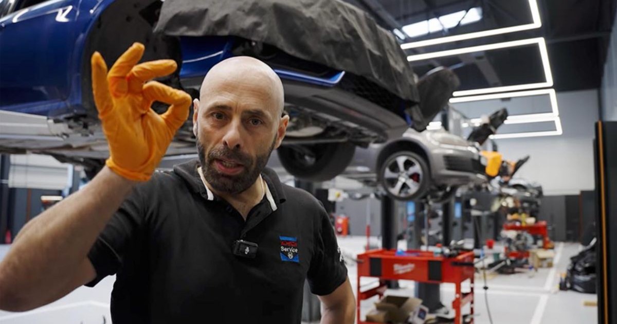 Un mecanic român într-un service auto, în spatele lui se vede o mașină suspendată în service