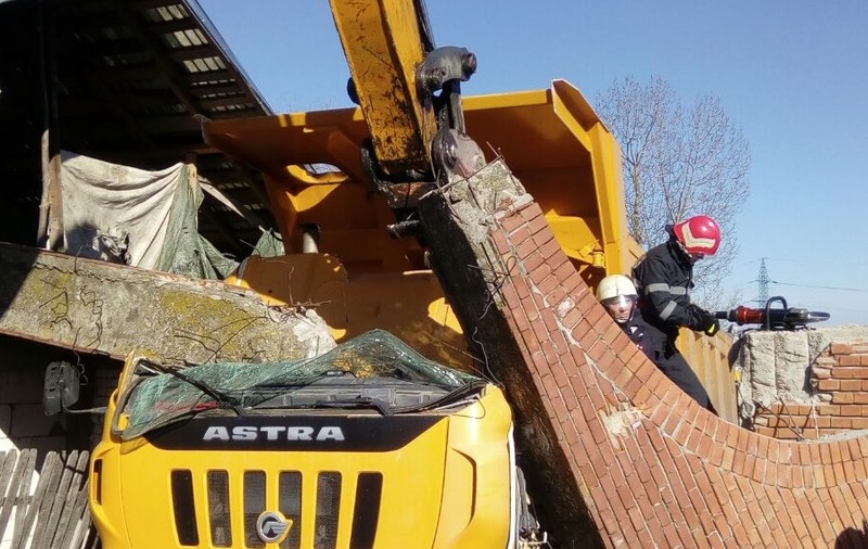 FOTO/Șoferul unei autobasculante, rănit după ce vehiculul a acroșat o poartă din beton care a căzut pe cabină