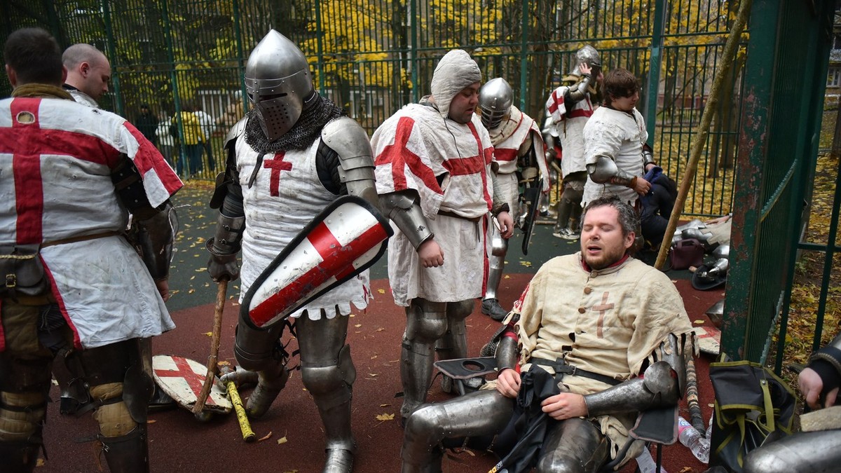 Oameni purtând componente de armură medievală iau parte la un eveniment de luptă amicală desfășurat pe un teren de baschet pentru a menține luptele de stradă medievale vii