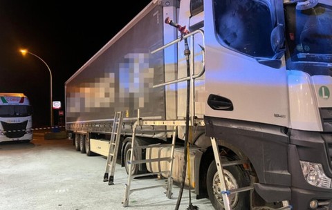 Un autotren alb oprit pe timp de noapte într-o parcare sau stație de serviciu, având o platformă metalică și o scară instalate lângă cabină pentru acces la înălțime.