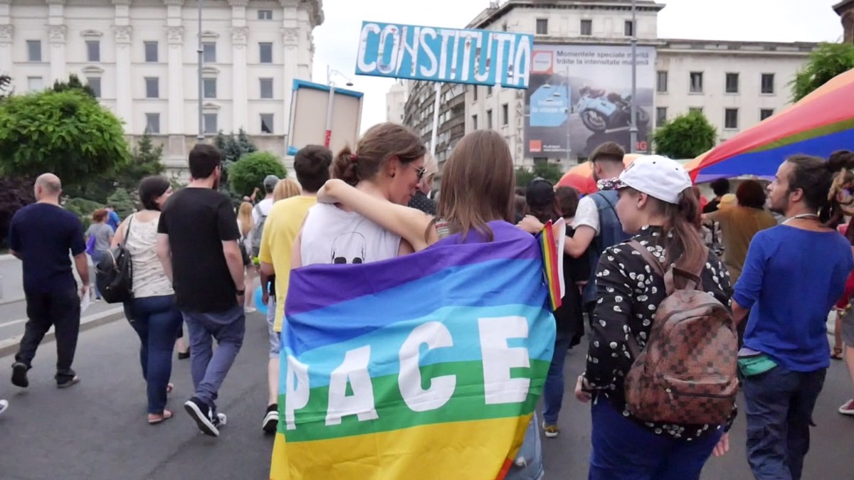 marșul gay din București. Două fete purtând pe spate un steag pe care scrie PACE