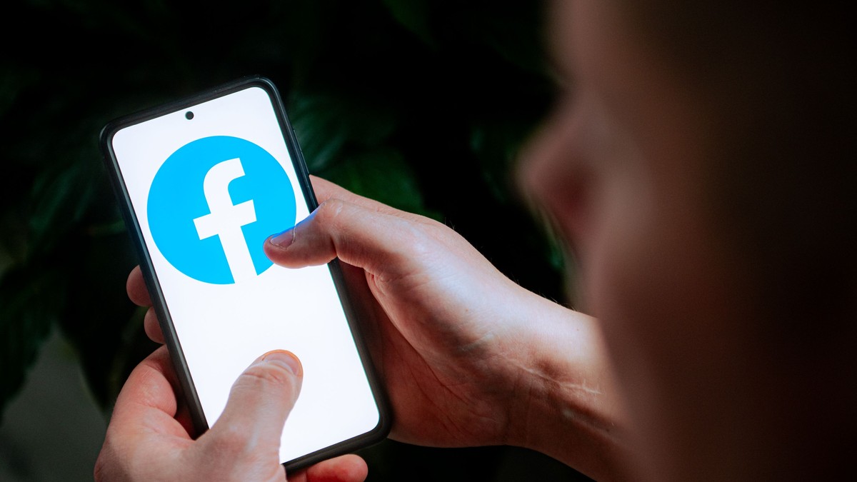 Bărbat care ține în mână un telefon pe ecranul căruia este afișat logo-ul Facebook.