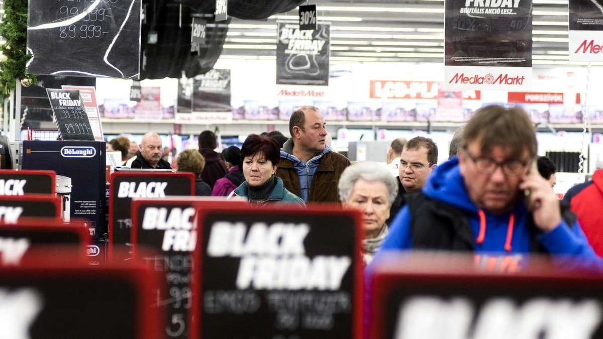 Black Friday, o afacere de 300 de milioane de euro în România. Oameni la coadă, cu semne de promoții privind Black Friday pe lângă ei