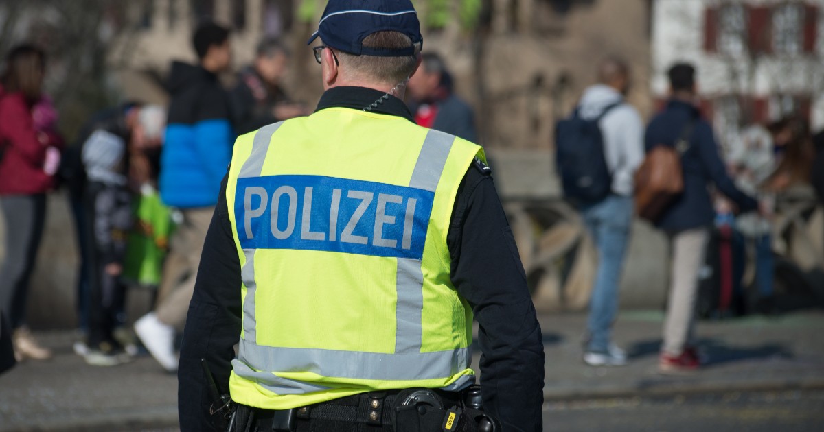 Un polițist care stă cu spatele și poartă o vestă pe care scrie POLIZEI