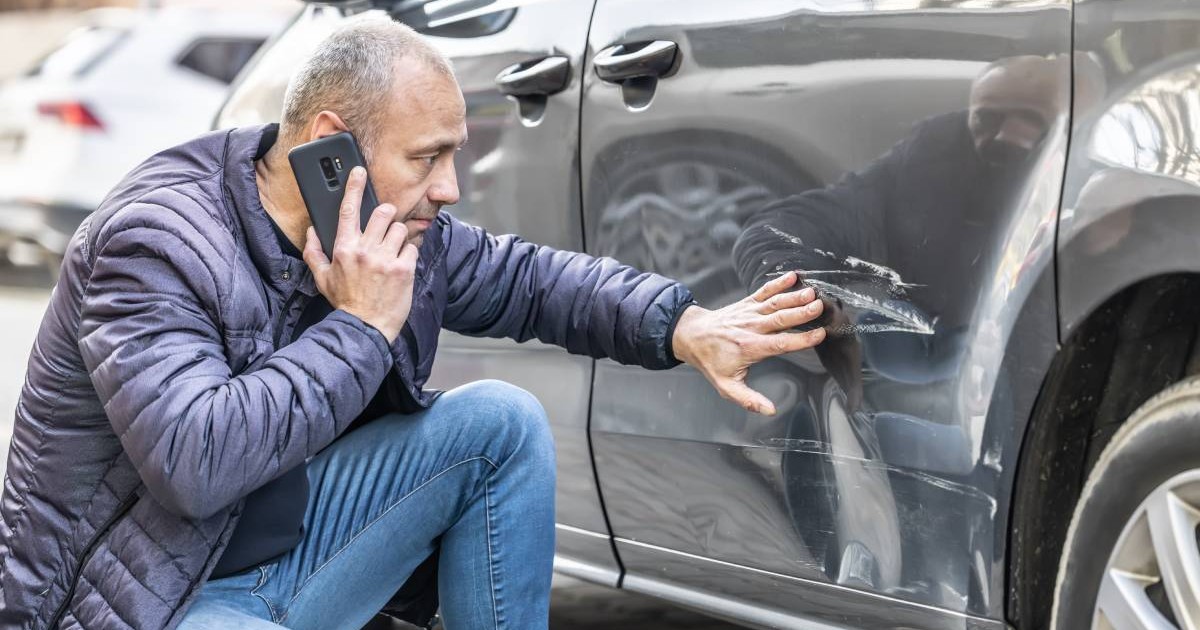 un barbat care sta langa masina lovita in parcare vorbind la telefon
