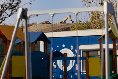 Chiar lângă gardul grădiniței lucrează un excavator
