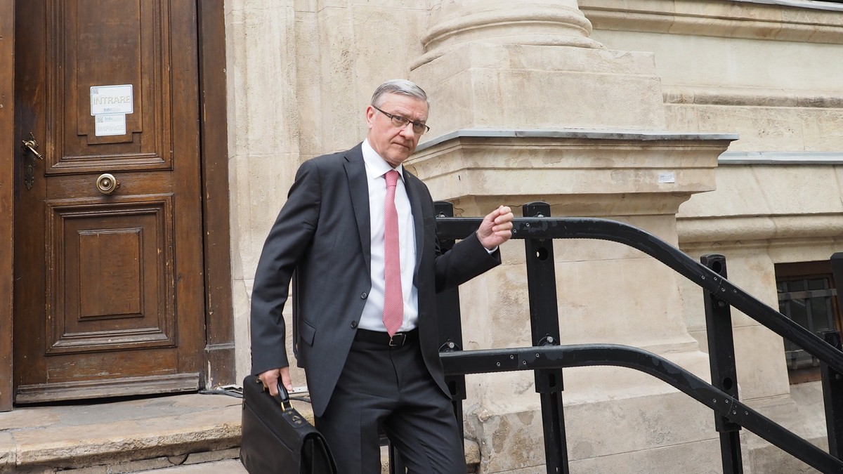Un barbat in costum negru si camasa alba cu cravata roz iese din tribunal