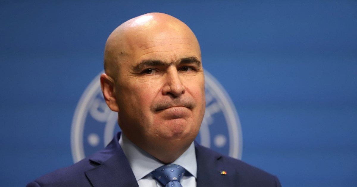 Premierul Ilie Bolojan, cu costum și cravată, îți mușcă buzele