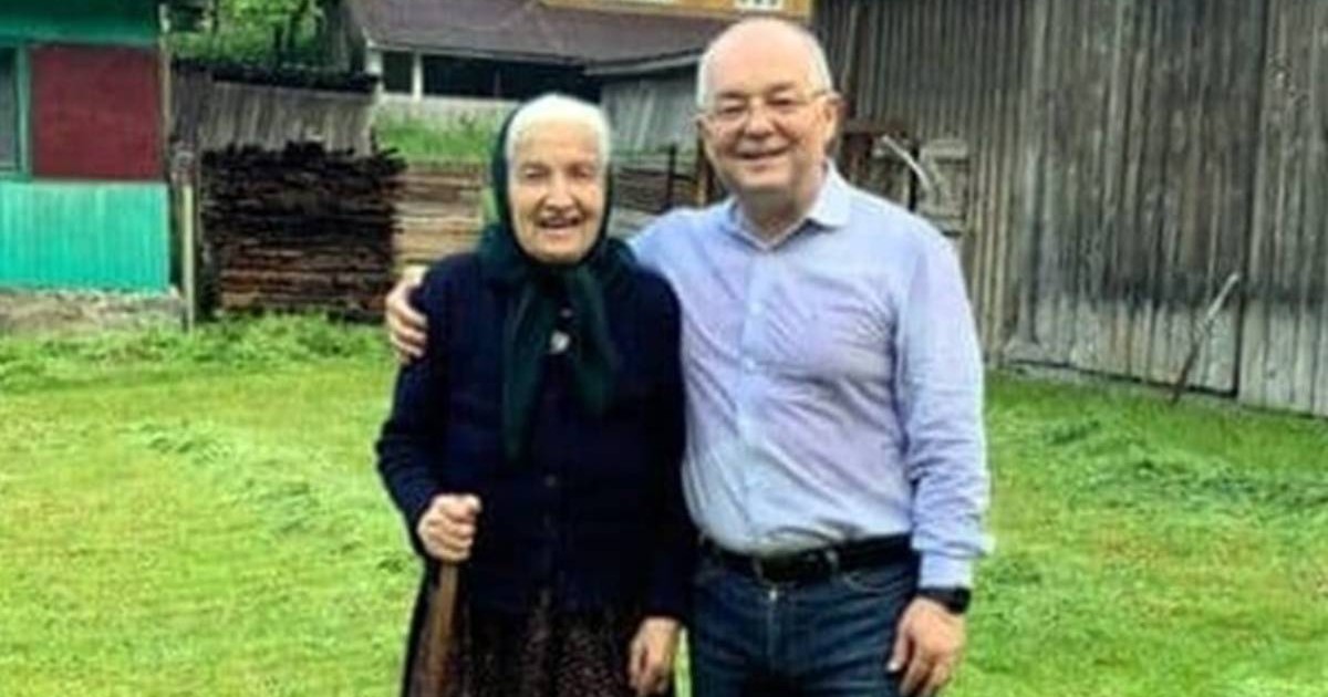 În imagine este primalul Emil Boc, in cămasă bleu, alaturi de mama sa Ana Boc, cu basma neagra pe cap, haine negre si un toiag in mana dreaptă, cei doi stau alaturi, afara, Emil Boc are mana dreapta in jurul mamei sale, se vede iarbă verde in spate si o casa batraneasca