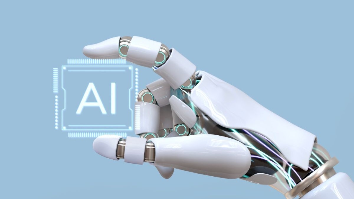 mână de roboțel care ține între degetul mare și degetul arătător un cip cu textul „AI”, pe fundal bleu