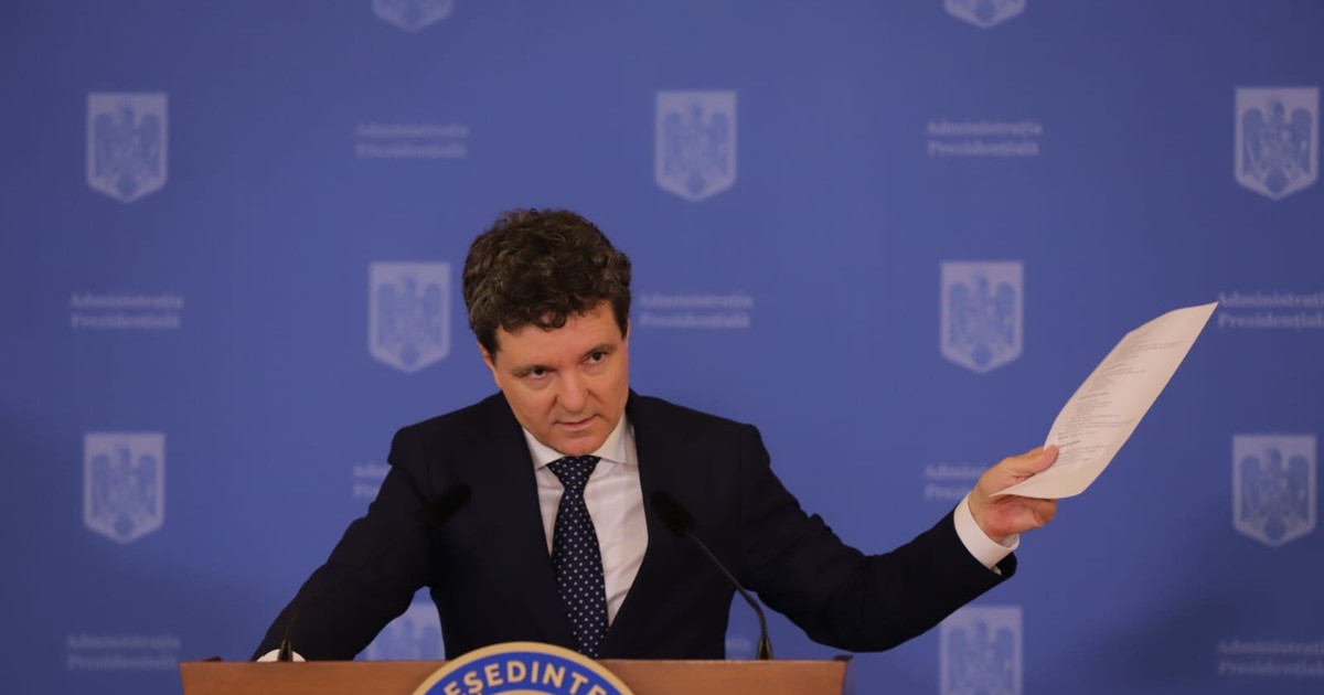 Nicușor Dan la pupitru, în conferința de presă din 14 iulie 2025, îmbrăcat într-un costum negru, cu o cămașă albă și o cravată neagră, având în mâna dreapta un document printat și ținând mâna stângă pe pupitru, cu capul ușor plecat