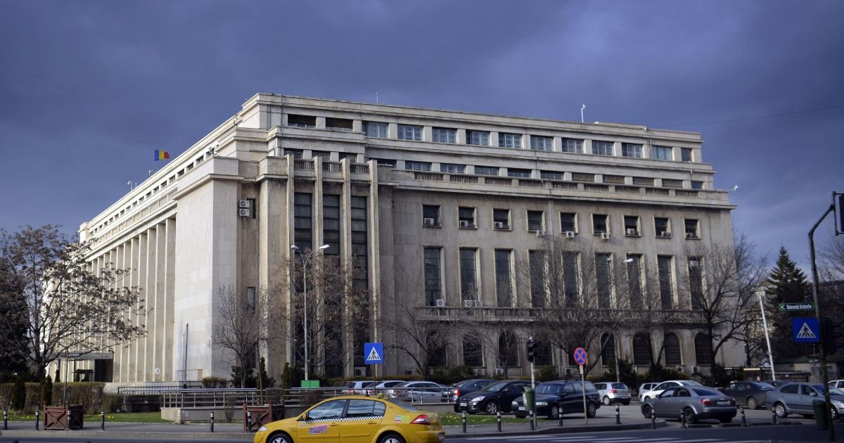 Imagine de ansamblu cu Palatul Victoria, cu mașini care trec prin Piața Victoriei, cu un cer închis