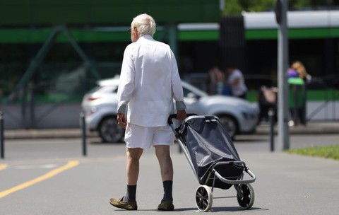 Un pensionar îmbrăcat în alb, fotografiat cu spatele, merge pe stradă cu un căruț de piață, în București, iulie 2026. Foto: Libertatea/ Dumitru Angelescu