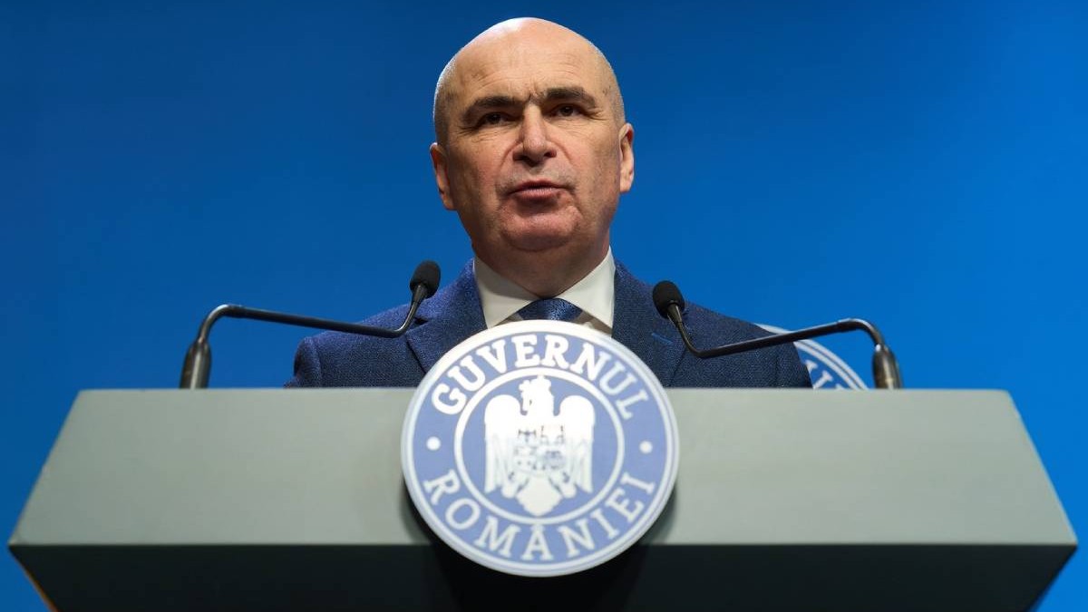 Ilie Bolojan, la pupitru cu sigla Guvernului Romaniei, fundal albastru