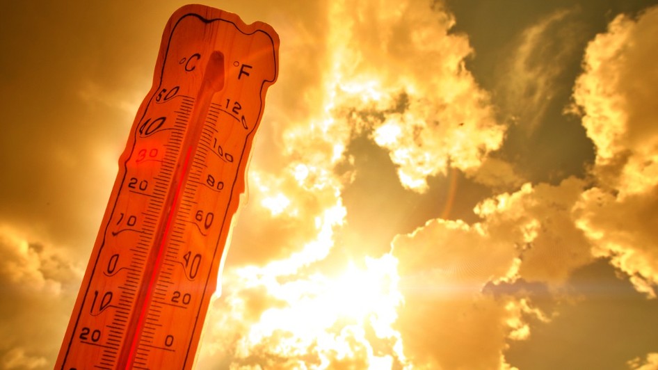 Un termometru ce indică o valoare ridicată de aproximativ 36 de grade Celsius, profilat pe un cer luminos de vară cu raze puternice de soare care creează un efect cald, portocaliu-auriu