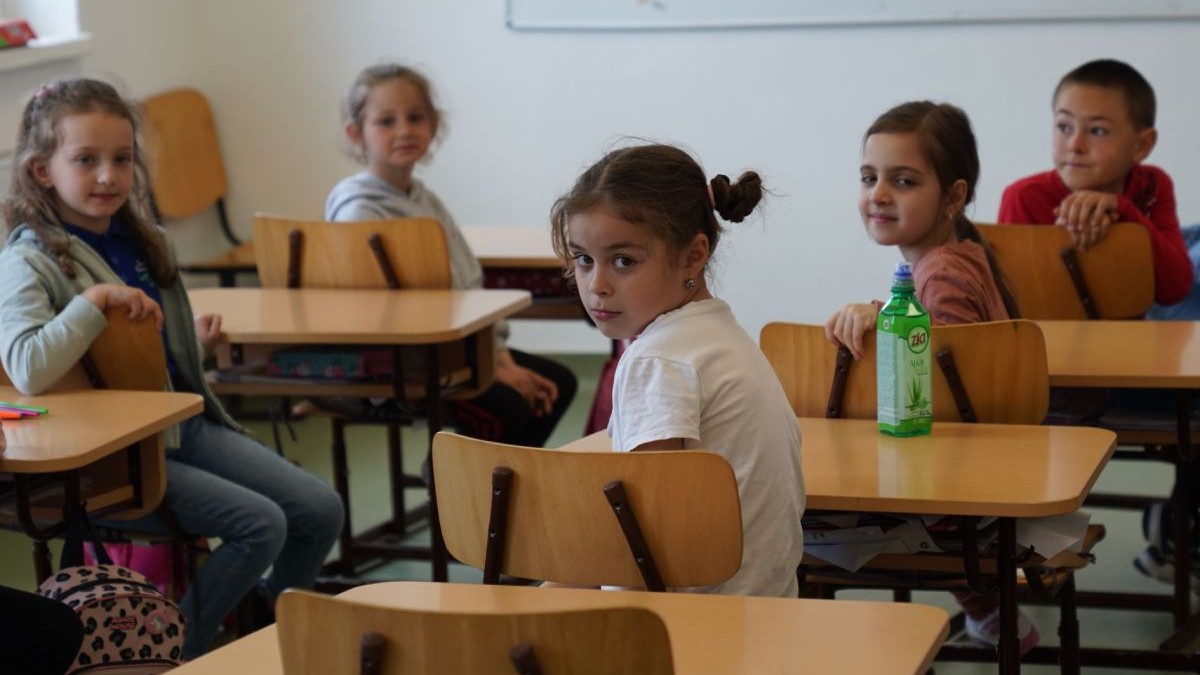 Copii în bănci, într-o sală de clasă dintr-o școală, cu bănci de lemn