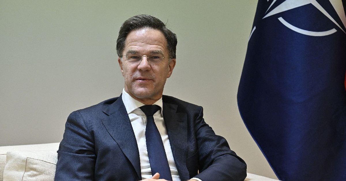 Mark Rutte, secretarul general al NATO, îmbrăcat în costum bleumarin, cămașă albă și cravată bleumarin. În spate, steagul NATO