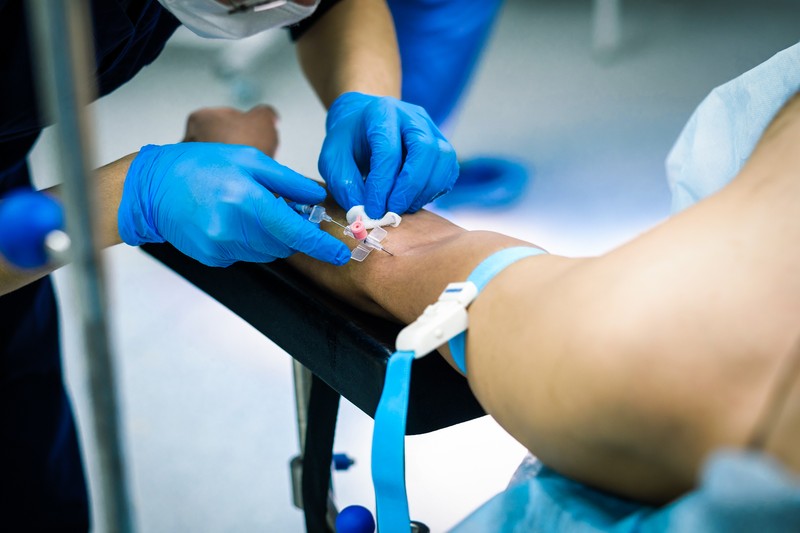 The doctor's hands in gloves stick a dropper needle into the patient's hand. Selective focus. A doctor in sterile gloves puts a catheter to the patient for intravenous administration of drugs.