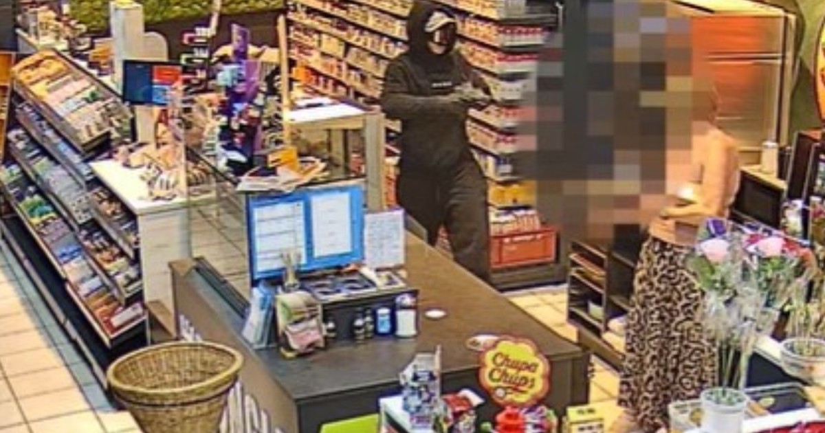 O imagine surprinsă de o cameră de supraveghere arată o persoană mascată și îmbrăcată în negru care comite un jaf armat într-un magazin, îndreptând o armă spre persoana de la casă.