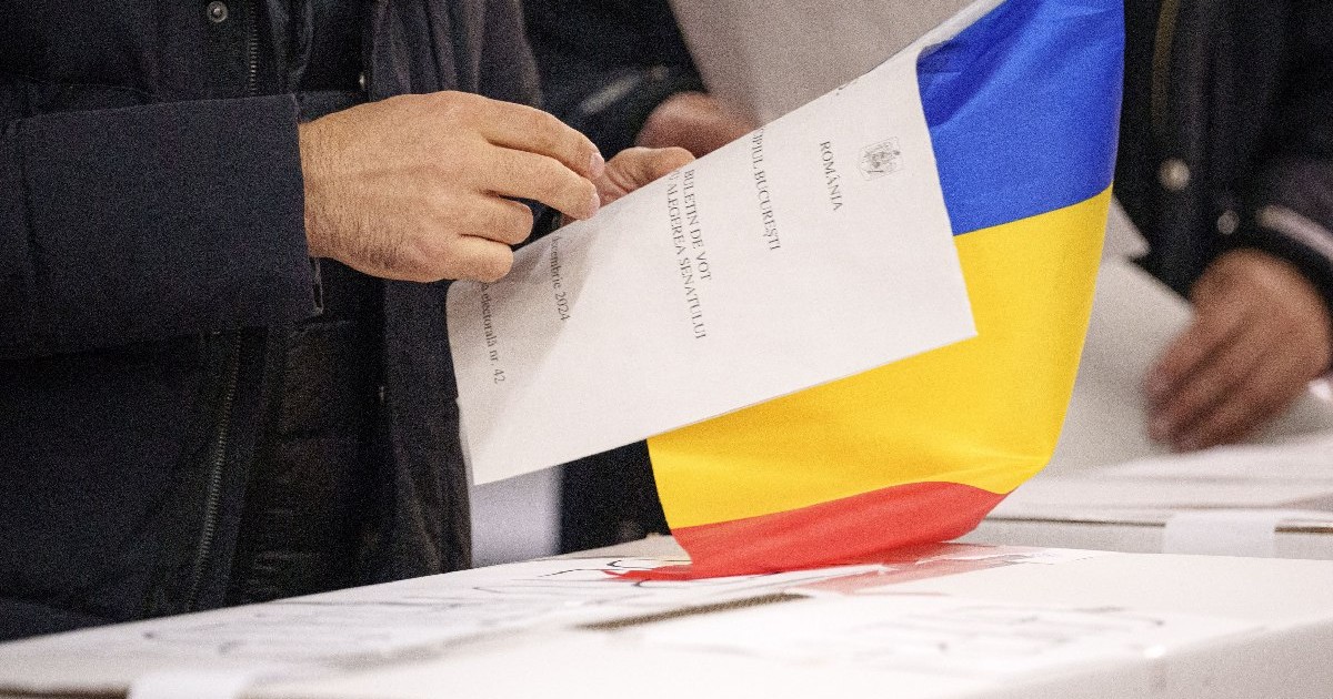 Un român are buletinul de vot, ștampila și drapelul țării într-o mână și se pregătește să bage în urnă hârtia pe care a votat