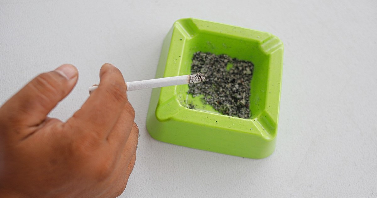 Țigară aprinsă într-o scrumieră verde pe fundal alb