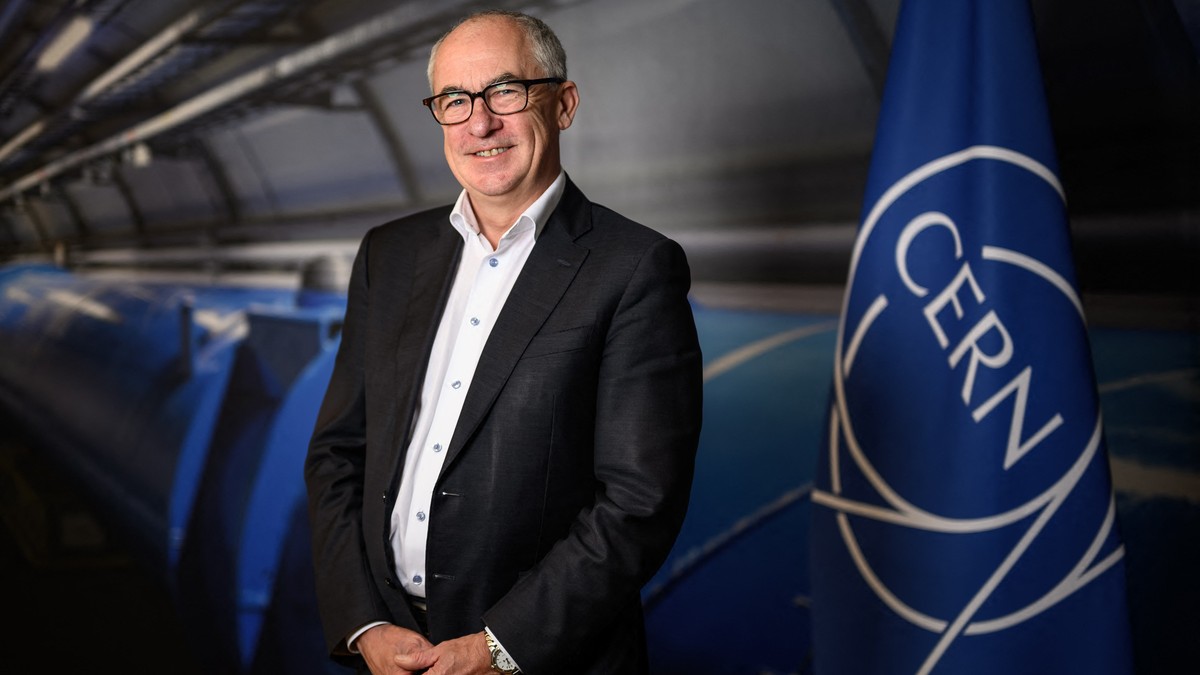 Mark Thomson, viitorul director general CERN stă lângă un steag albastru cu logo-ul organizației.