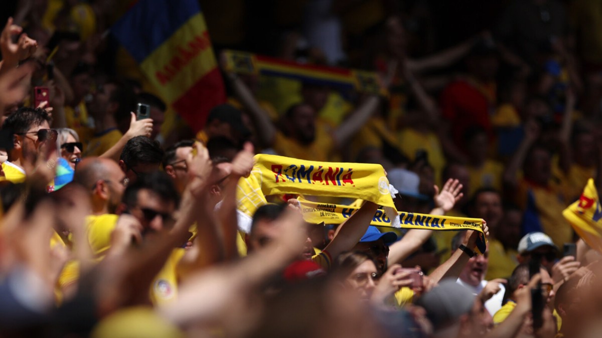 În imagine se văd suporteri români îmbrăcați în galben, aflați în tribune, fluturând eșarfe și steaguri tricolore.