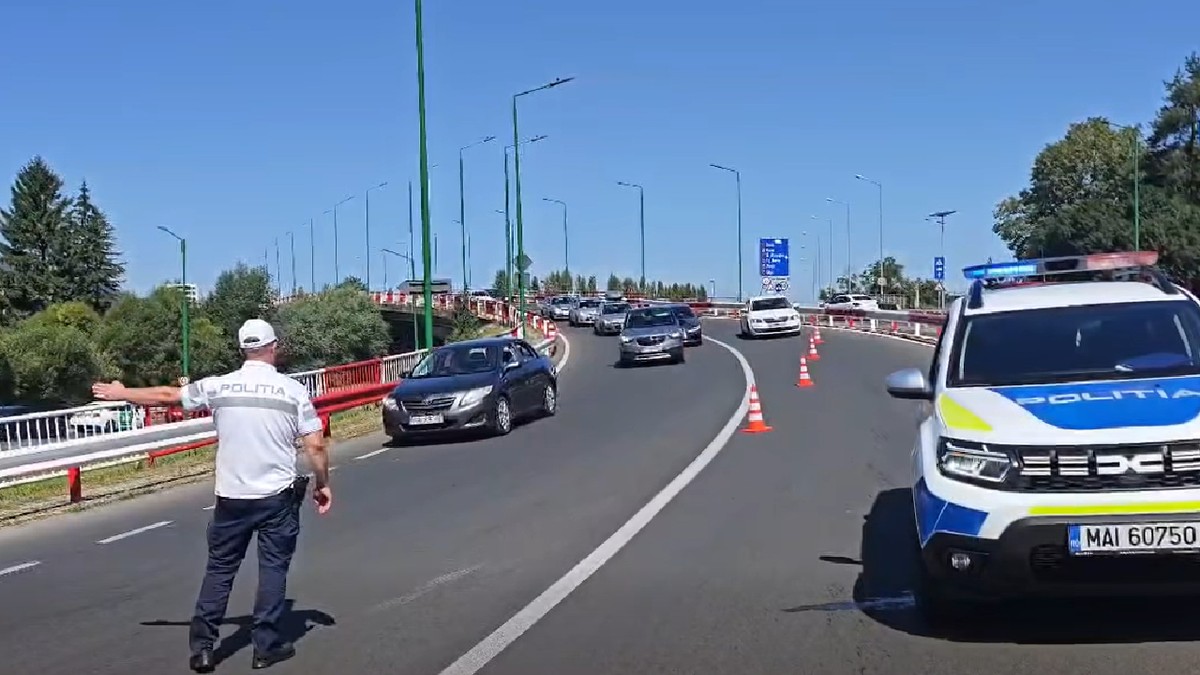 Coloană de mașini dirijată de un polițist, se vede și mașina de poliție