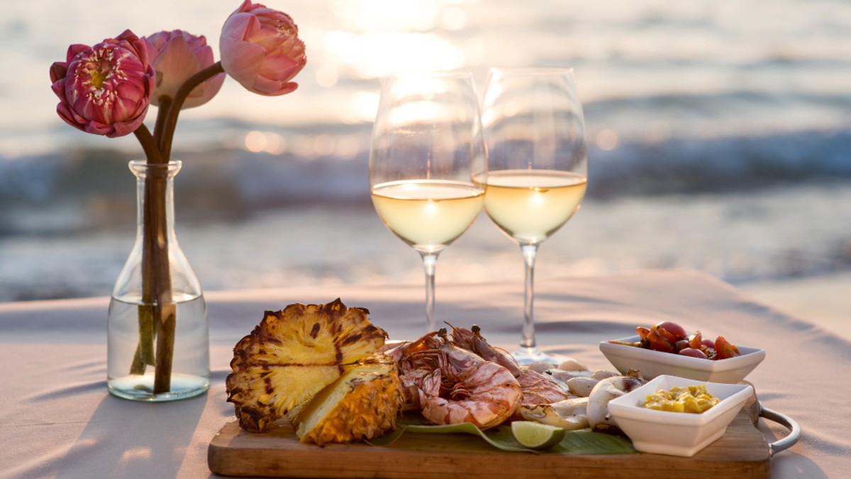 Câte tipuri de vin alb există - Cină romantică la restaurant pe plajă cu vedere la apusul soarelui.