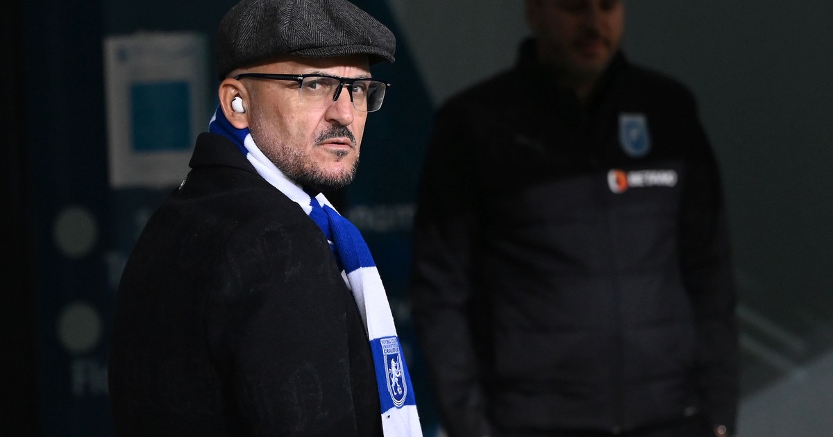 Imagine cu Adrian Mititelu. Poartă un palton negru și o eșarfă în culorile echipei FC U Craiova. Pe cap poartă o șapcă de culoare închisă