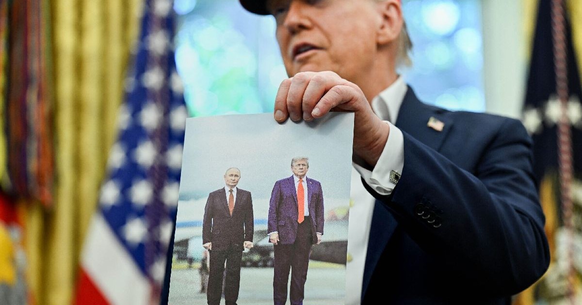 Donald Trump are o șapcă roșie pe cap și ține în mâna stângă o fotografie cu el și Vladimir Putin, la Anchorage, în Alaska