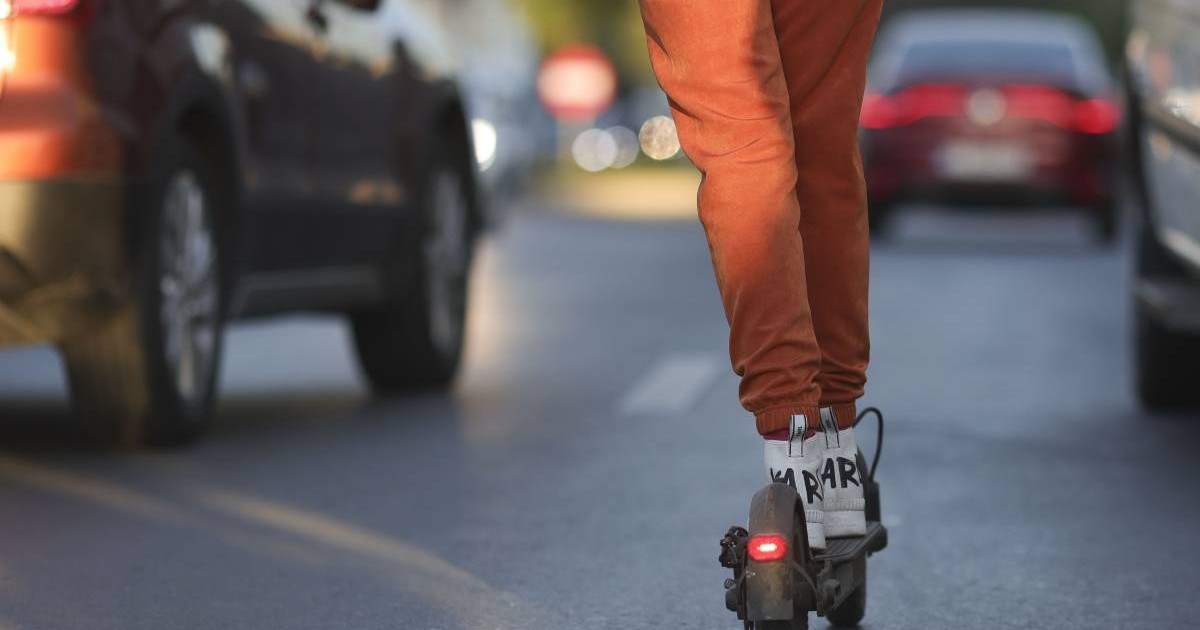 persoana imbracata cu pantaloni portocalii pe o trotineta electrica printre masini aflate in trafic