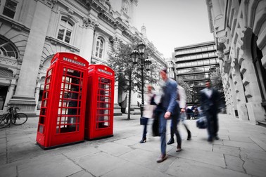 Business life concept in London, the UK. Red phone booth, people in suits walking