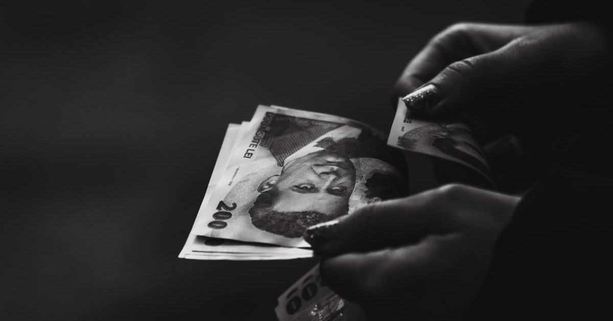 Mâna unei femei care numără bancnote românești de 200 de lei, pe un fundal negru