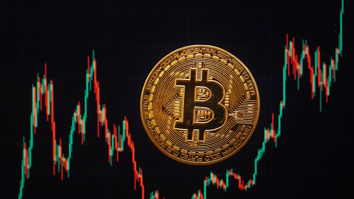 O monedă Bitcoin se află pe un ecran care arată cursul de schimb Bitcoin - dolar american.