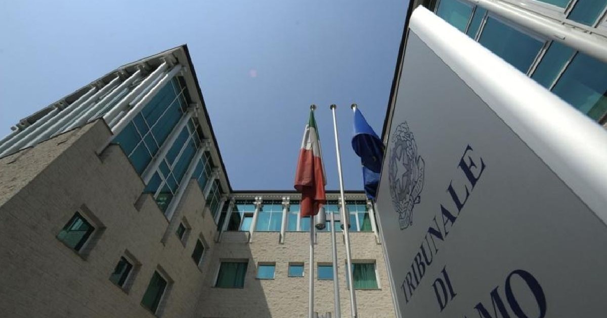 Imaginea prezintă clădirea Tribunalului din Bergamo, Italia, cu steagurile Italiei și Uniunii Europene în centrul fotografiei