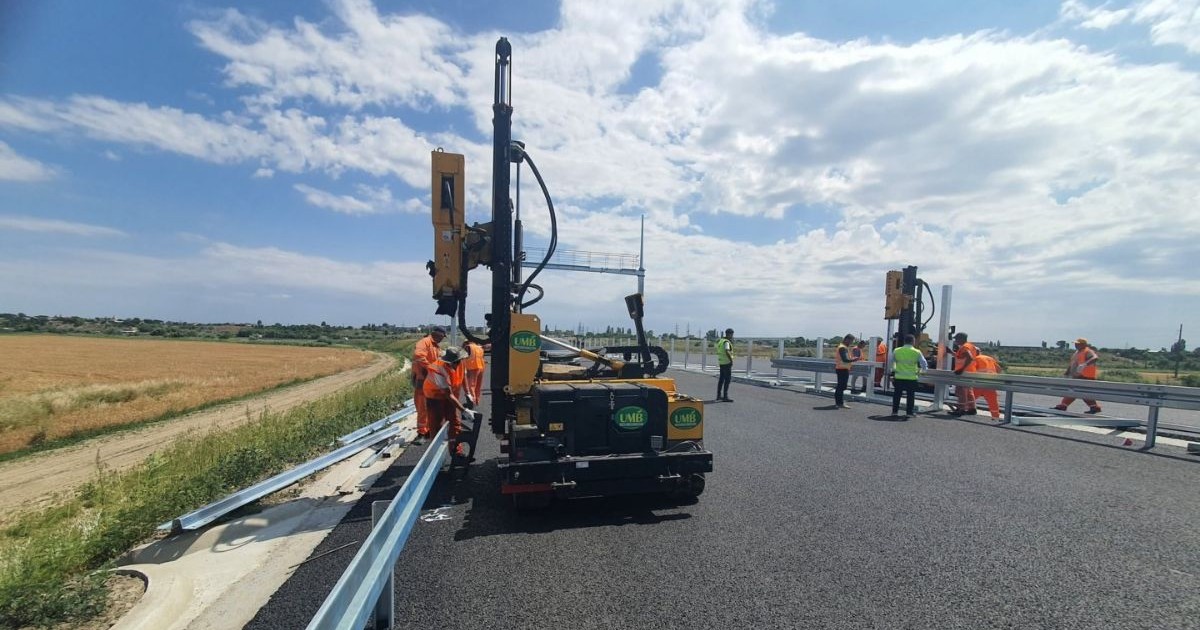 Muncitori montează parapeți pe drumul expres brila-galati, nou asfaltat, cu utilaje grele, în câmp deschis.