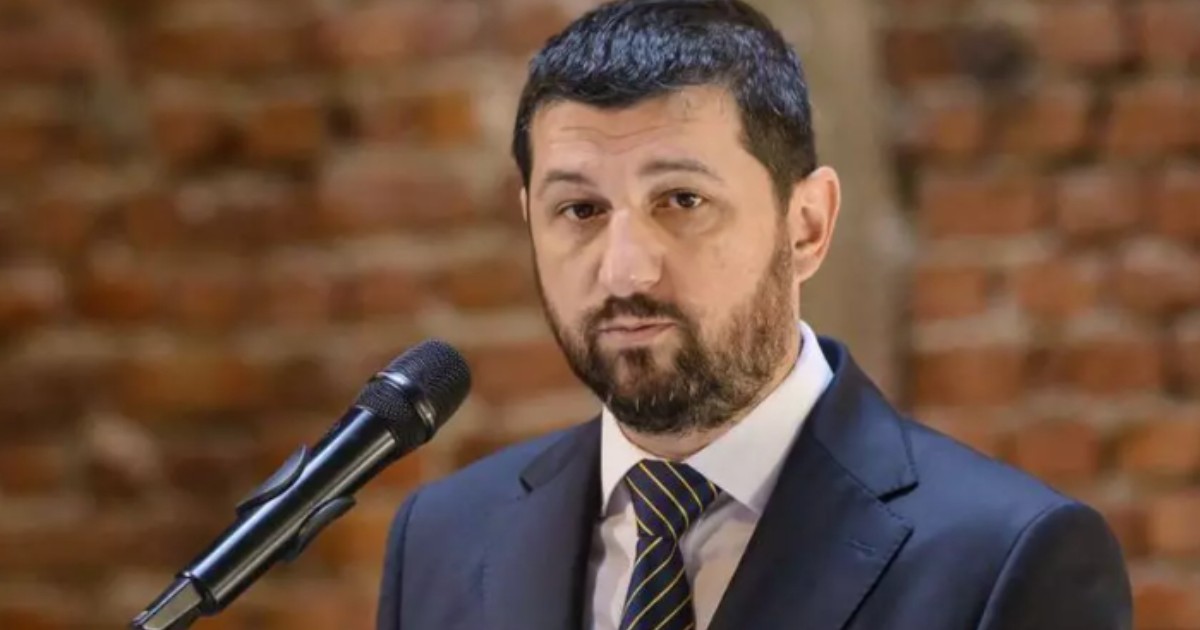 În imagine este ilustrat Marius Lulea, îmbrăcat în costum negru, poartă o cămașă albă și o cravată. Acesta se află în fața unui microfon.