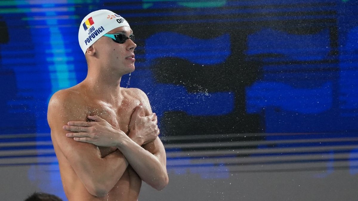 David Popovici, cu ochelari de înot și cască pe cap, lângă bazinul de concurs la Campionatele Europene de Natație 2026 din Paris, cu fundal albastru și negru
