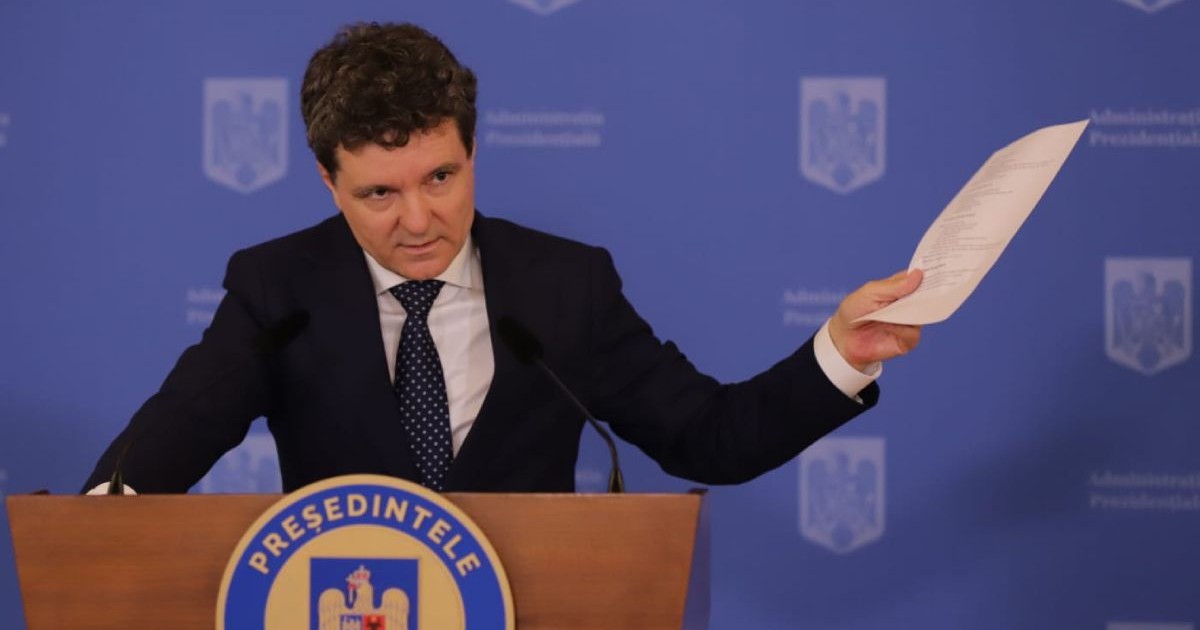 Nicușor Dan, îmbrăcat în costum negru și cămașă albă, la pupitrul Administrației Prezidențiale, pe fundal albastru