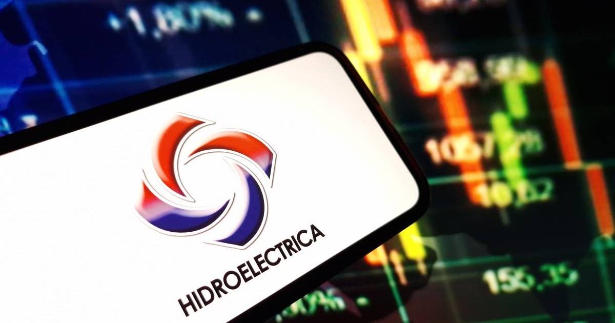 Un telefon pe ecranul căruia apare logo-ul de la Hidroelectrica, iar în spatele lui se vede ecranul unui laptop unde sunt publicate cifre referitoare la consumul din facturile de energie