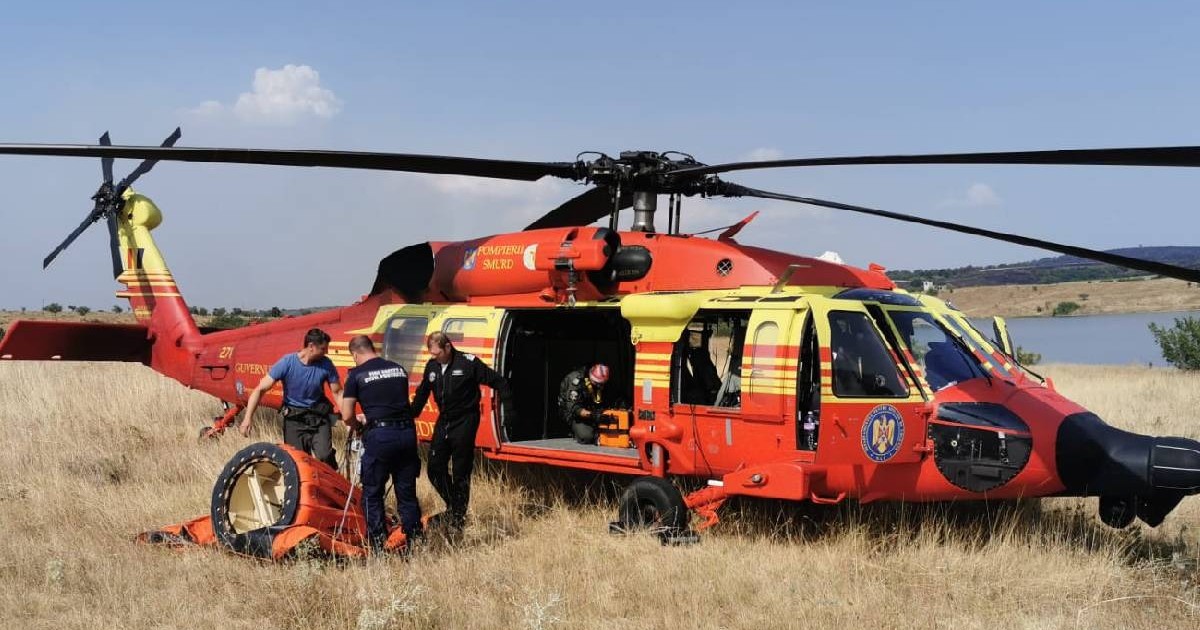 Imagine cu un elicopter al pompierilor pe un câmp. În imagine se văd și trei salvatori