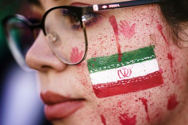 O protestatară poartă vopsea roșie pe față și emblema națională a Iranului în timpul unui protest de solidaritate față de moartea tinerei Mahsa Amini din Iran, 7 octombrie 2022, în Berlin.