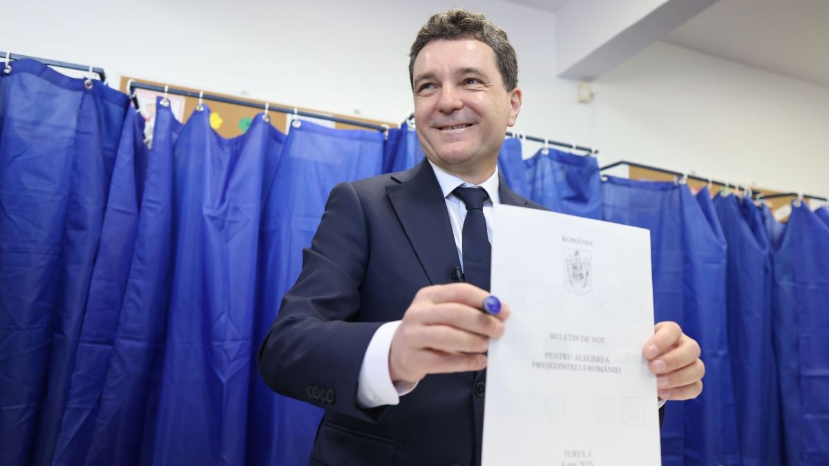 Nicosor Dan în costum inchis la culoare si cămasă albă introduce buletinul de vot in urnaă, in spatele lui perdele albastre de la cabina de vot