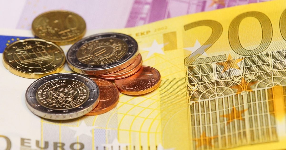 Prim-plan cu bancnote de 200 de euro și mai multe monede euro, împrăștiate deasupra. În fundal se vede o bancnotă euro estompată, parțial vizibilă.