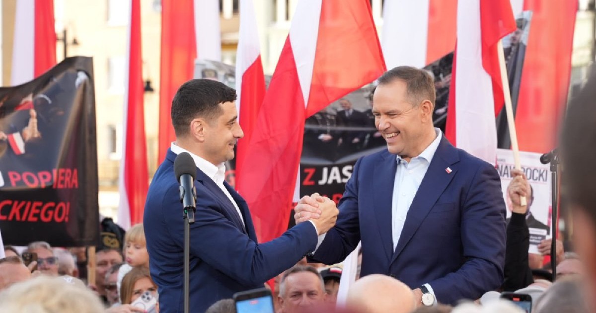 George Simion și Karol Karol Nawrocki dau mână pe o scenă, în timpul unui miting electoral din Polonia, sunt înconjurați de steaguri alb/roșii