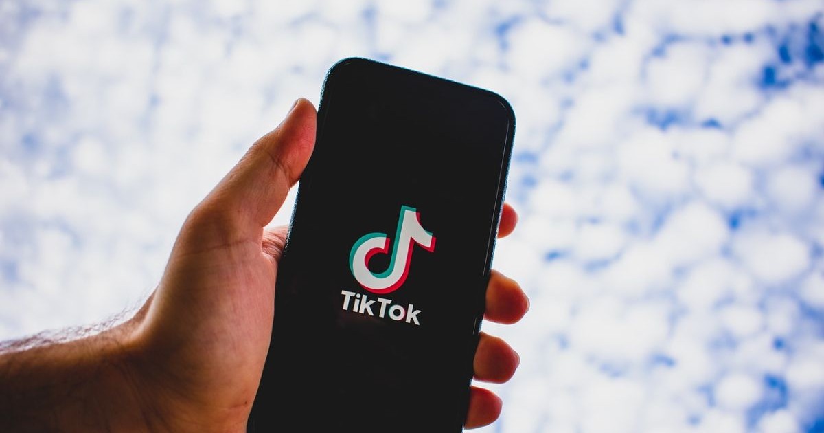 Un bărbat ține în mână un telefon , pe ecranul căruia este TikTok și apare sigla acesteia. Foto: pixabay.com