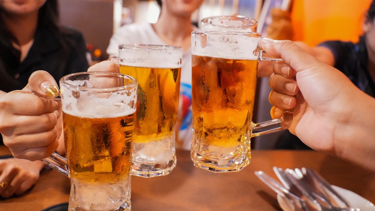 Imaginea surprinde mai multe persoane ciocnind halbe cu bere într-un local, într-o atmosferă relaxată și convivială. Paharele pline cu bere sunt ridicate pentru un toast, sugerând un moment de socializare între prieteni.